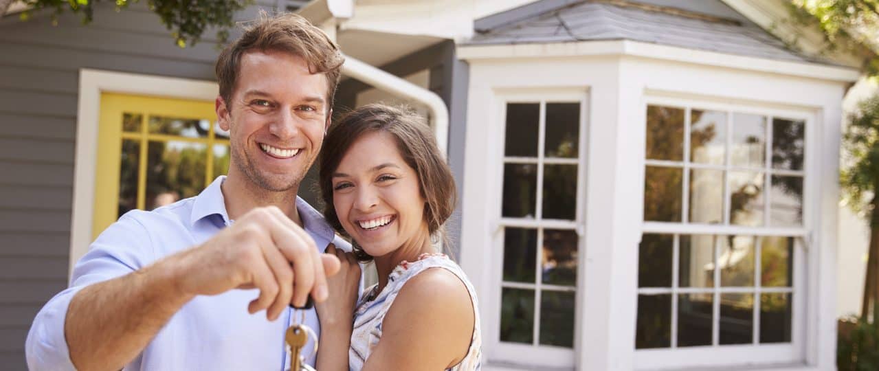 Couple With Keys Standing Outside New Home
